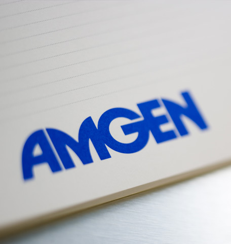 Notizblock mit blauem Amgen-Logo, fotografiert auf einem Bürotisch.